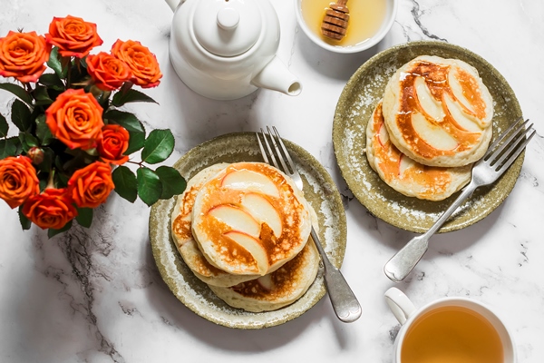 breakfast served pancakes with apples green tea a bouquet of roses on a light marble background top view - Оладьи постные с яблоками