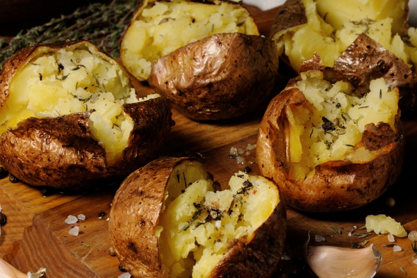 broken baked potato with spices and herbs on a wooden board - Картофель печёный