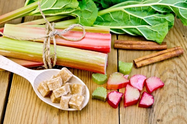 bundle of stalks rhubarb cut pieces of rhubarb with a sheet and a knife a spoon of sugar cubes cinnamon on a wooden board - Маседуан из ревеня