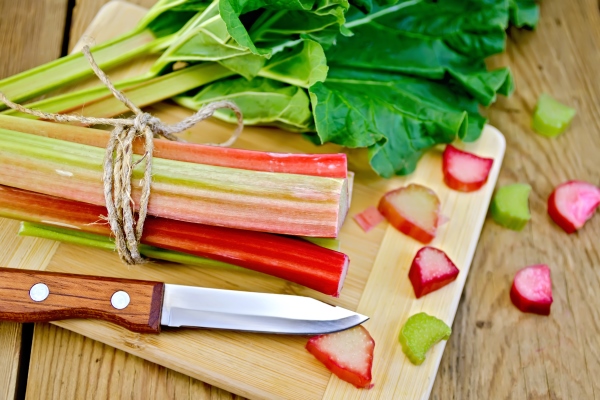 bundle of stalks rhubarb rhubarb pieces with a sheet and a knife on a wooden board - Икра из ревеня с кабачками и баклажанами