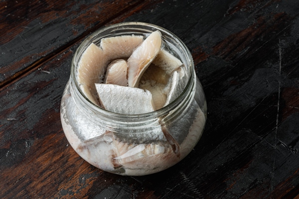 canned wild herring fillets in glass jar on old dark wooden table - Сельдь по-домашнему