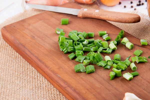 close up view of cut green onion with knife on cutting board on sackcloth background - Суп из сныти со свежими огурцами