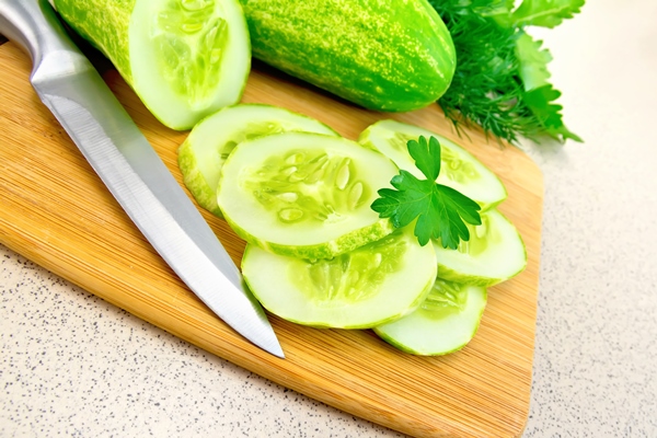 cucumbers cut with parsley and a knife on a wooden board dill on the background of a granite table - Салат из капусты и огурцов
