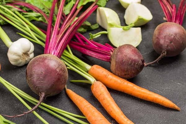 fresh beets with tops close up carrots with stalks and chopped kale turnip cabbage black background top view - Свекольная икра с чесноком