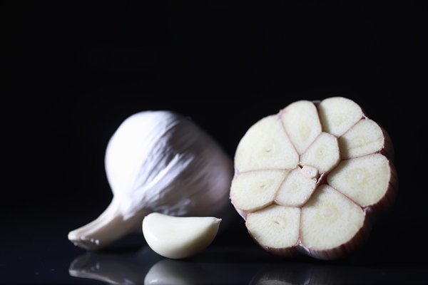 fresh garlic clove on black background garlic is rich in vitamins useful spring good spices garlic sliced on a dark background raw sliced garlic - Рагу из картофеля с красным сладким перцем и капустой