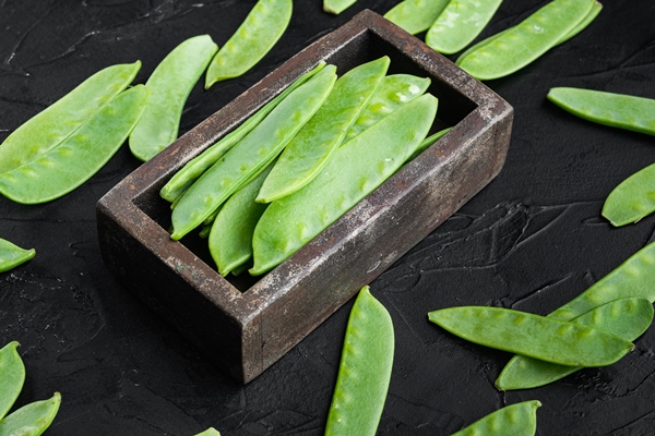 fresh organic mangetout also known as sugar snap pea set in wooden box on black stone background - Суп весенний, постный стол
