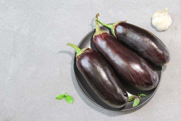 fresh raw purple eggplants on a ceramic black plate with purple and green basil on stone background - Баклажаны припущенные