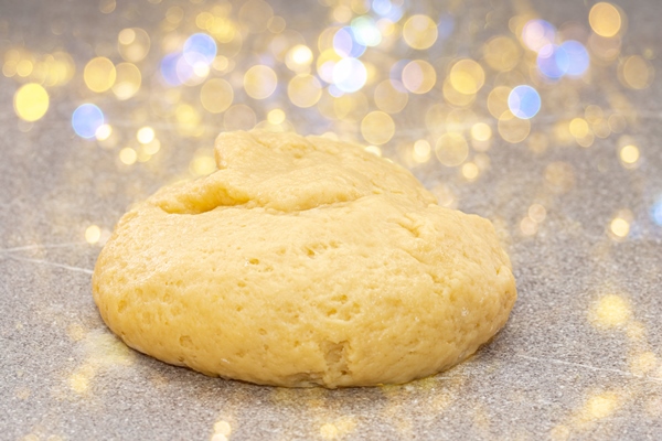 fresh yellow raw dough in the shape of a ball for baking gingerbread men for christmas on a fabulous background with yellow bokeh christmas food tradition concept - Пресное тесто для пирожков