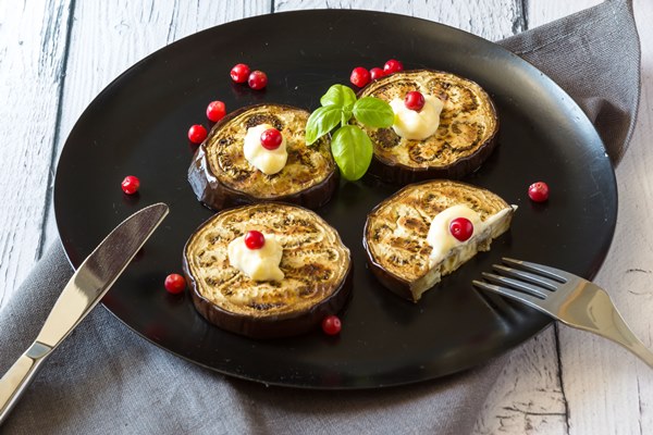 fried eggplant and cranberries garnished with basil leaves on a dark plate over wooden background - Баклажаны с чесноком, постный стол