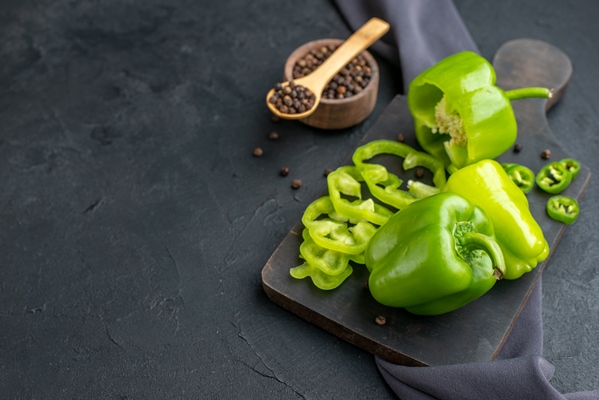 front view of whole cut chopped green peppers on wooden cutting board on dark color towel on black surface - Картофельный салат с рисом и рыбой