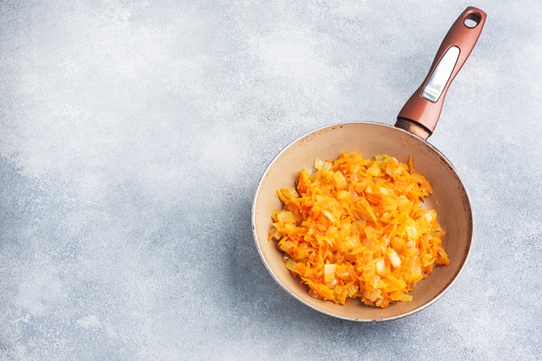 fry grated carrots and chopped onions with oil in a frying pan gray concrete background copy space - Постный картофельный суп с перловкой и грибами