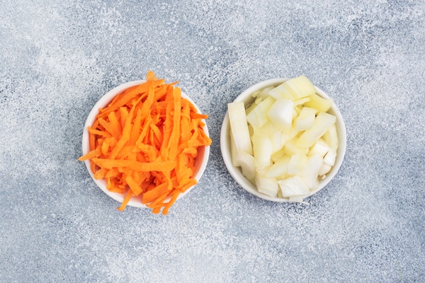 grated carrots and chopped onions in a white plate raw vegetables ingredients for roasting gray table copy space top view - Постный суп грибной с галушками