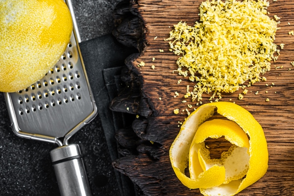 grated lemon zest and spiral peel on wooden board black background top view - Пудинг из риса с черносливом