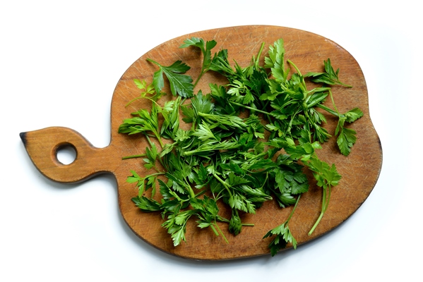 green chopped parsley leaves on a wooden cutting board on a white background - Тушёный картофель с черносливом и изюмом