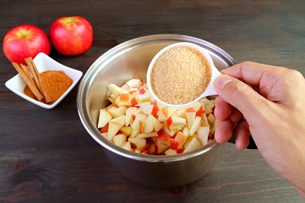 hand adding a cup of unrefined sugar into the pot of diced fresh apples for making apple compote - Тушёные яблоки