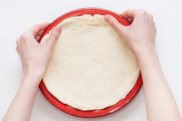 hands stretching the dough on a plate - Слоёный сладкий русский пирог