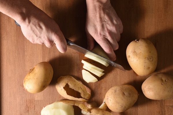 high angle view of a cook cutting a potato in a wood - Тушёный картофель с черносливом и изюмом