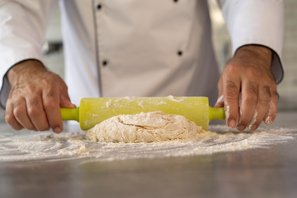 male chef in the kitchen rolling dough - Пирог с кислой капустой и грибами