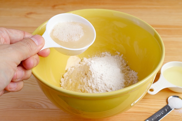 man s hand pouring yeast with water into the bowl of flour - Штрудели с яблоками