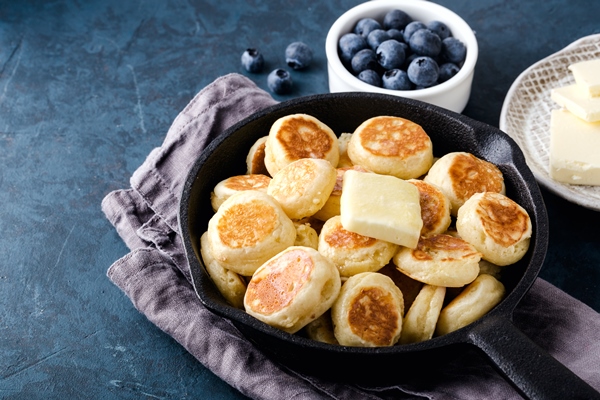 mini cereal pancakes in cast iron frying pan on grey napkin blueberry dark blue cement background top view - Сырники из нежирного творога