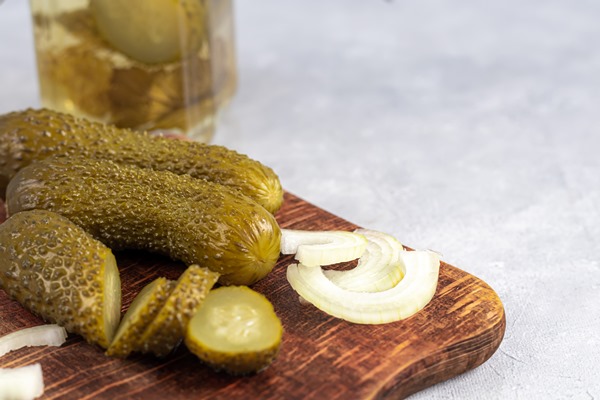 pickled cucumbers in a glass jar and on a wooden board fermented food on a gray background copy space - Салат из лука и солёных огурцов