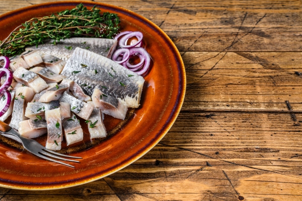 pickled marinated herring fish sliced fillet on a plate with thyme and onion wooden background top view copy space - Сельдь с жареным луком