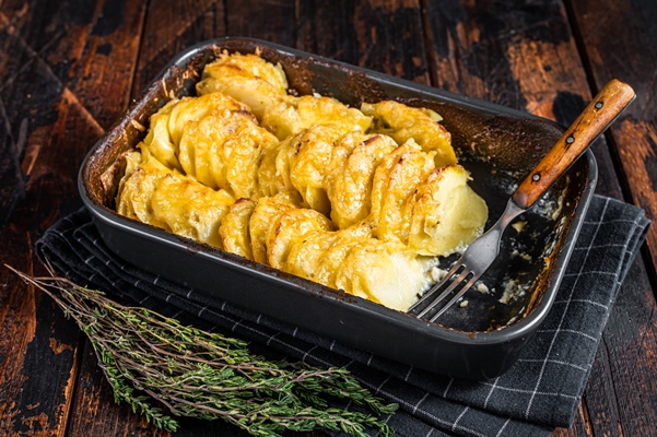 potato casserole gratin dauphinois in a baking dish dark wooden background top view - Картофель ломтиками, запечённый с селёдкой