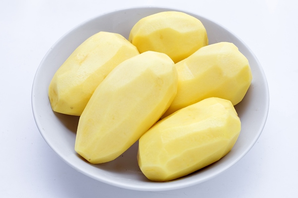 raw peeled potatoes in white bowl on white background - Картофель в кляре с грибным соусом