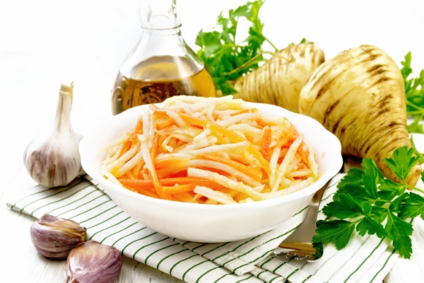 salad of fresh carrots parsnip and garlic with vegetable oil in a plate on napkin fork parsley and root vegetables on background of light wooden board - Суп из свежих грибов, постный стол