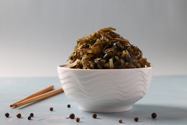 seaweed salad or kelp in transparent bowl on light blue table background healthy eating food - Маринованный лук с морской капустой