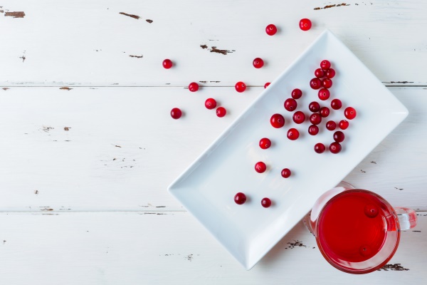 selective focus on cranberries in a fresh drink in a glass cup on a white wooden background fresh ripe berries are scattered on a white rectangular ceramic plate copy space flat lay - Салат из красной капусты в маринаде