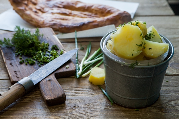side view boiled potatoes with green onions and bread and knife in table on wooden table - Винегрет картофельный с зелёным луком