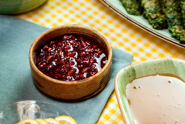 side view of pomegranate sauce in bowl and and honey on the table - Картофель с орехами и гранатом
