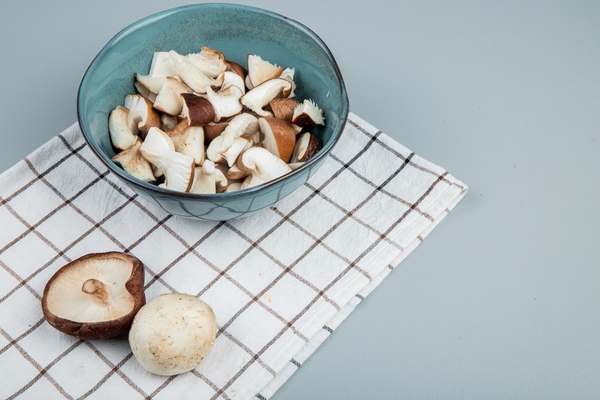 side view of sliced mushrooms in a bowl on plaid napkin on light blue - Постный суп из свежих грибов с овощами