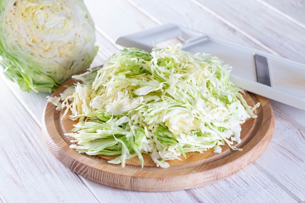 sliced fresh cabbage on a cutting board with a grater on a white wooden background - Суп с корневищами иван-чая