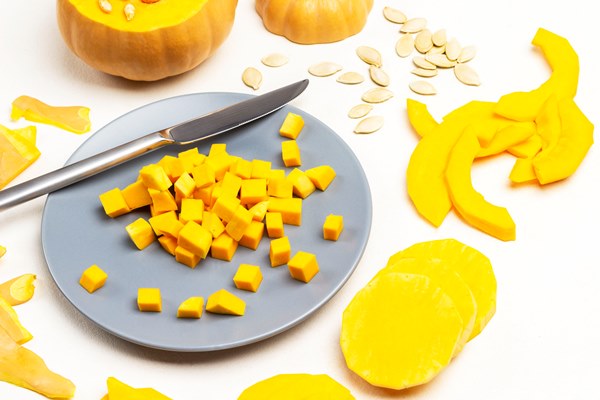 small pieces of pumpkin and knife on gray plate sliced pumpkin and seeds on table white background top view - Тыква жареная, постный стол