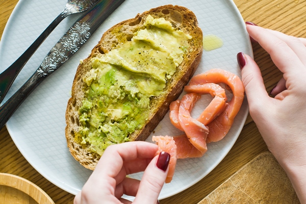 the chef lays out the salmon on toast with avacado on a black toast of bread - Сэндвич с авокадо и красной рыбой
