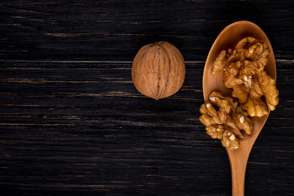 top view copy space peeled walnuts in a wooden spoon and in shell on a black wood background - Салат из тыквы