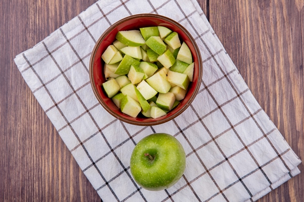 top view of fresh whole apple with chopped apple slices on red bowl on checked tablecloth and wood - Тыквенный кисель