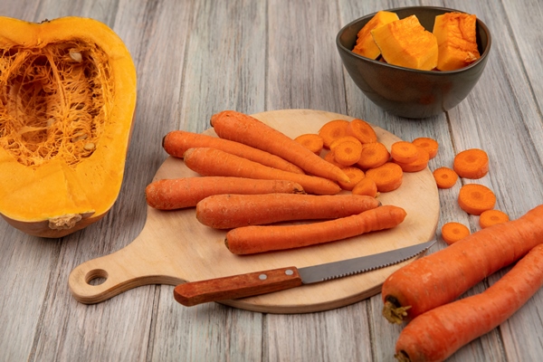 top view of healthy vegetable carrots on a wooden kitchen board with chopped carrots with knife with half pumpkin on a grey wooden background - Икра овощная по-селянски