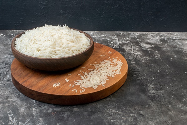 top view of perfect long rice in a brown bowl and on wooden board on gray background - Пудинг из риса с яблоками и вареньем