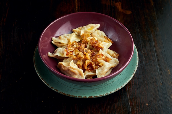traditional ukrainian dumplings filled with cabbage and fried onions served in a red bowl on a black background - Вареники с капустой