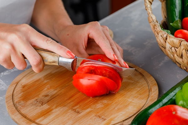 woman slicing tomato on a cutting board high angle view on a gray surface - Бутерброд с яйцом и помидорами