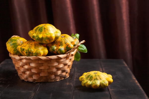 yellow patissons or squash in a wicker basket and a basil leaf on a brown wooden background - Картофель с патиссонами