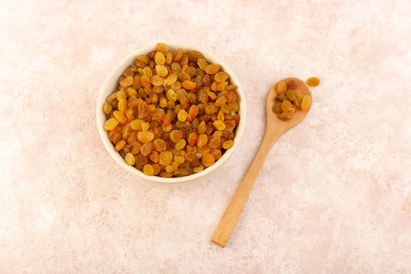 a top view orange dried raisins inside white round plate with wooden spoon on pink - Сочиво рисовое с миндалём и миндальным молоком