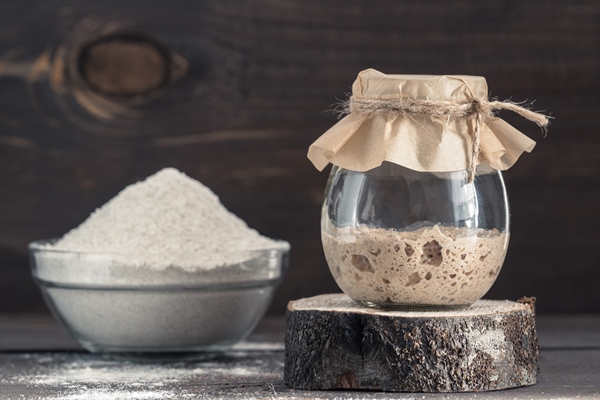 active rye sourdough starter in glass jar and rye flour on brown wooden background starter for sourdough bread toned image copy space - Серафимин квас