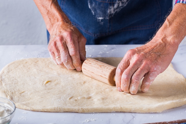 baking eating at home healthy food and lifestyle concept senior baker man cooking kneading fresh dough with hands rolling with pin spreading the filling on the pie on a kitchen table with flour - Гречневый хлеб в духовке