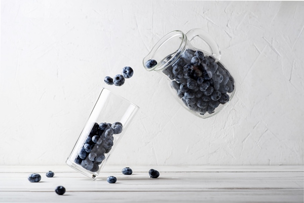 blueberry levitation blueberries from a jug are poured into a glass beaker on a white background making a berry smoothie abstract creative concept - Черника без сахара в бутылках (по Н. Г. Астравлянчик)
