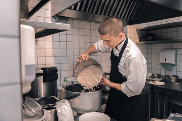 boiling rice young hard working chef wearing black apron of the cafeteria boiling rice for lunch - Коливо из риса