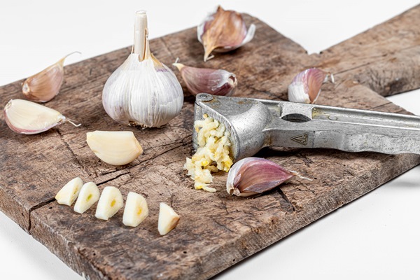 bulbs of garlic on old cutting board garlic press and cloves of garlic - Драники с овсяными хлопьями